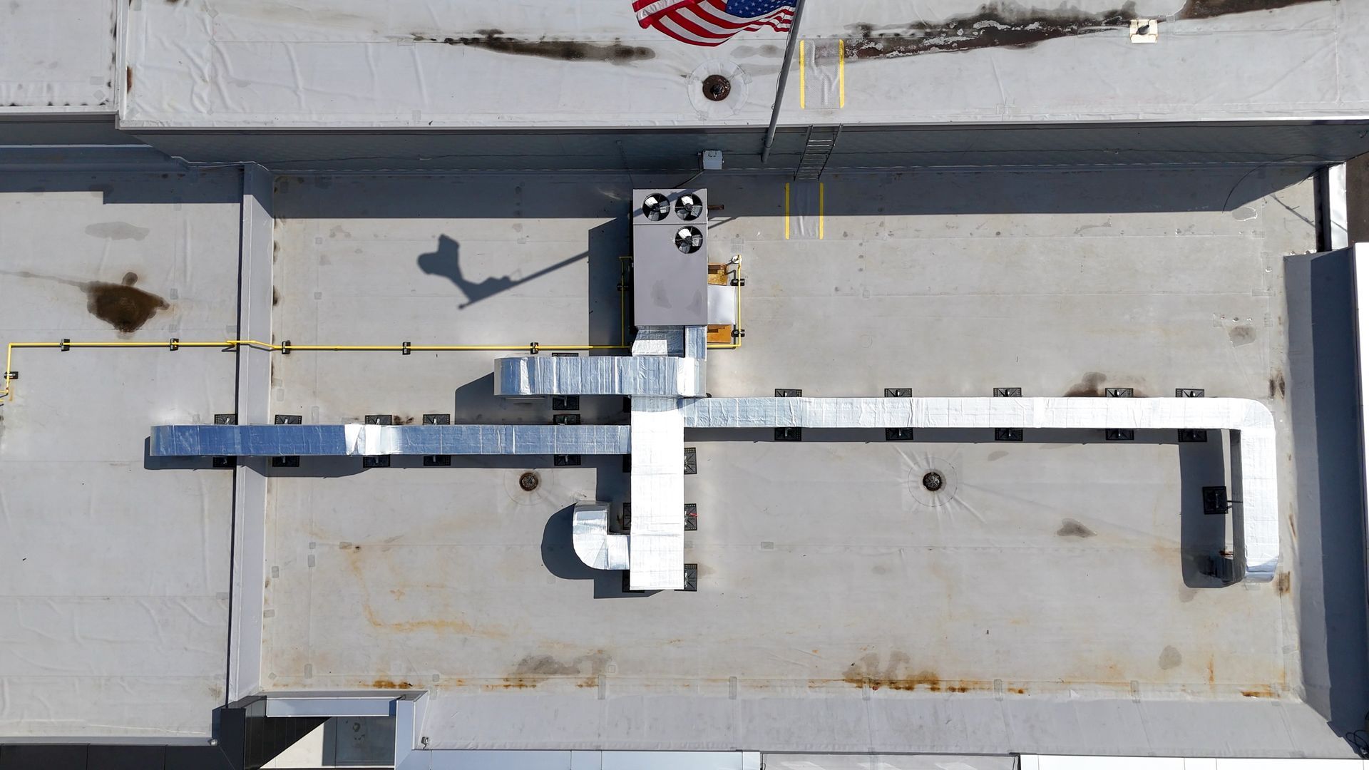 Overhead view of a gray structure with a metal duct system attached, American flag in the top right corner.