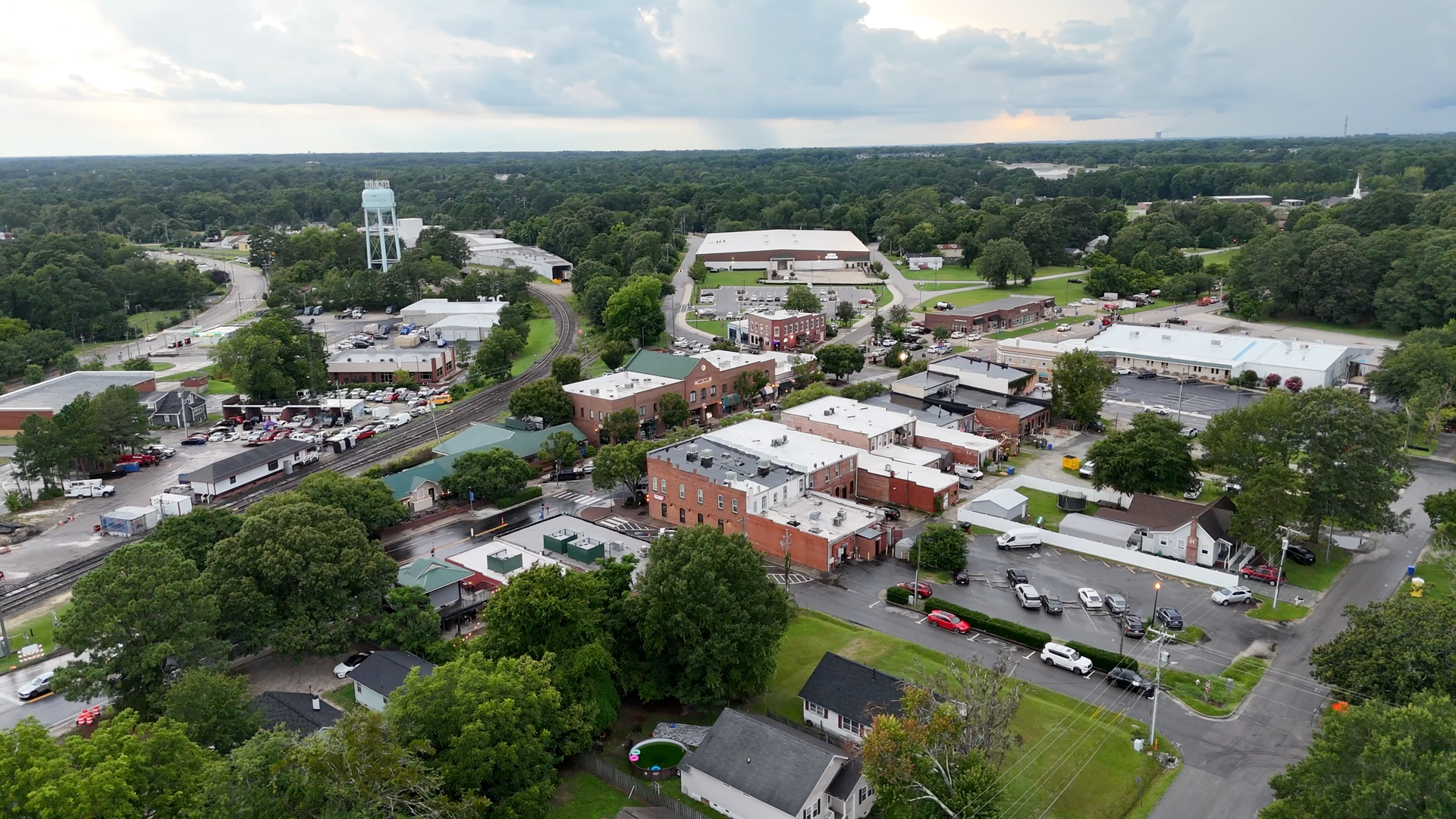 Aerial view of a small town with red brick buildings, green trees, and a water tower under a cloudy sky.