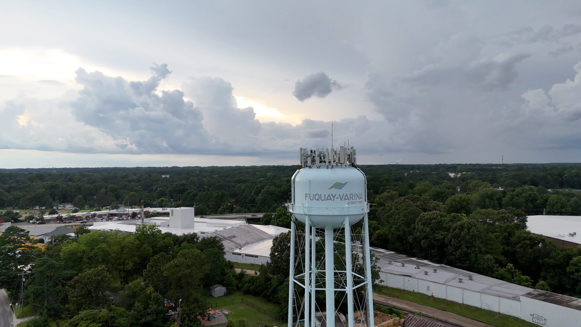 Water tower in front of a stormy sky, with surrounding buildings and trees visible in the background.