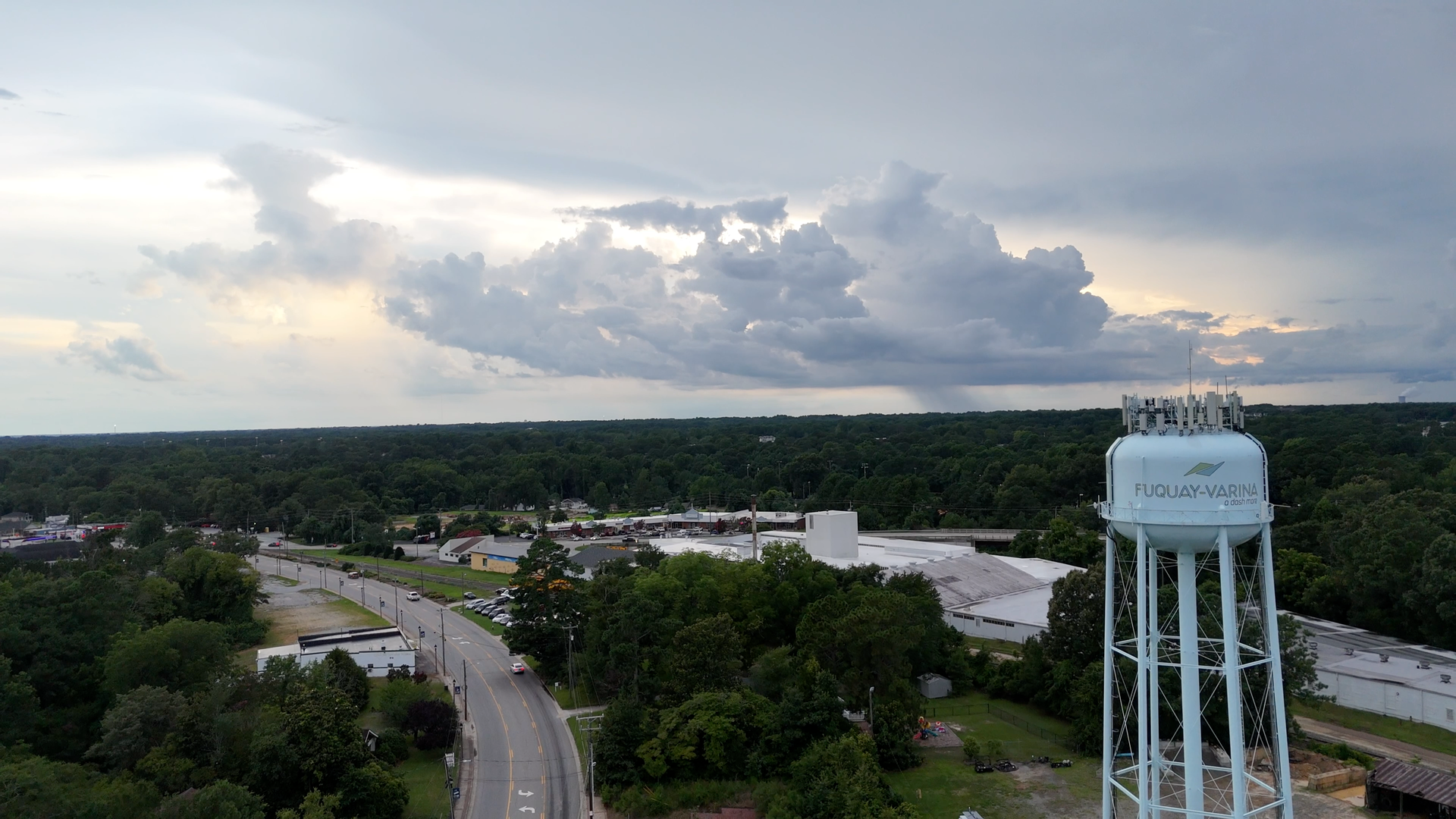 Water tower in Wilmington, NC under cloudy sky. Road and trees in the foreground.