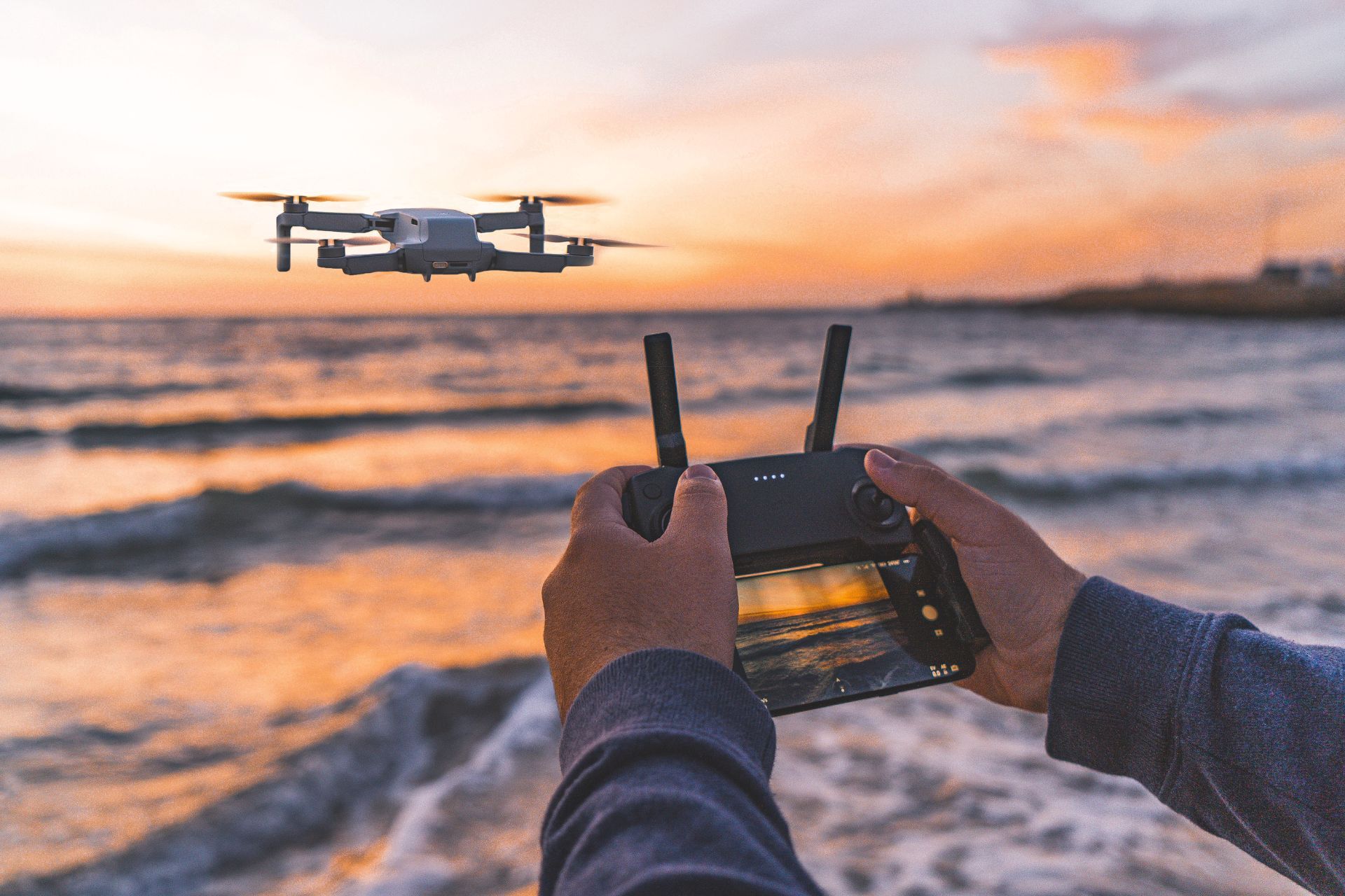 Person operating a drone above the ocean at sunset.
