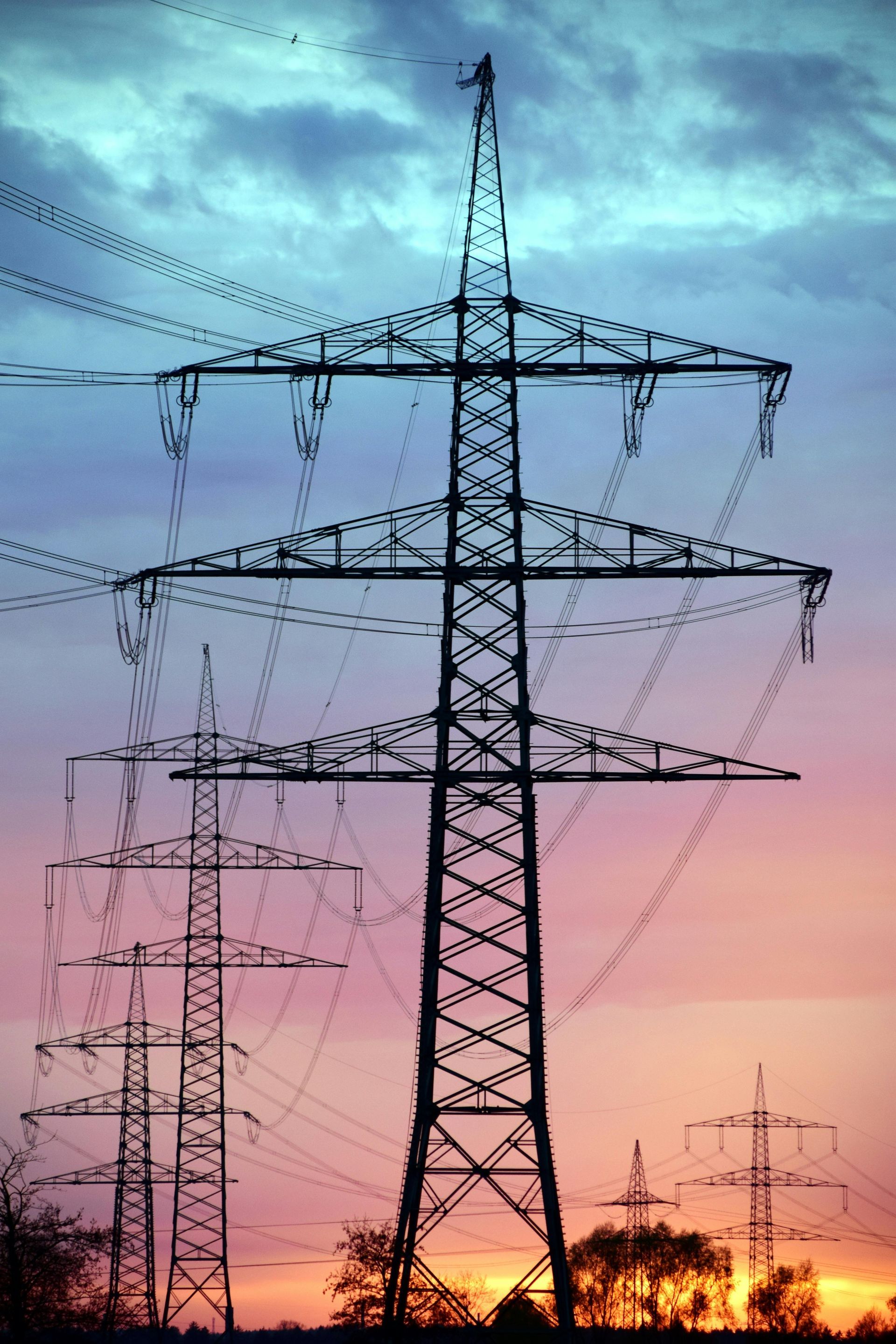 Power lines against a colorful dusk sky, silhouettes of pylons in a row.