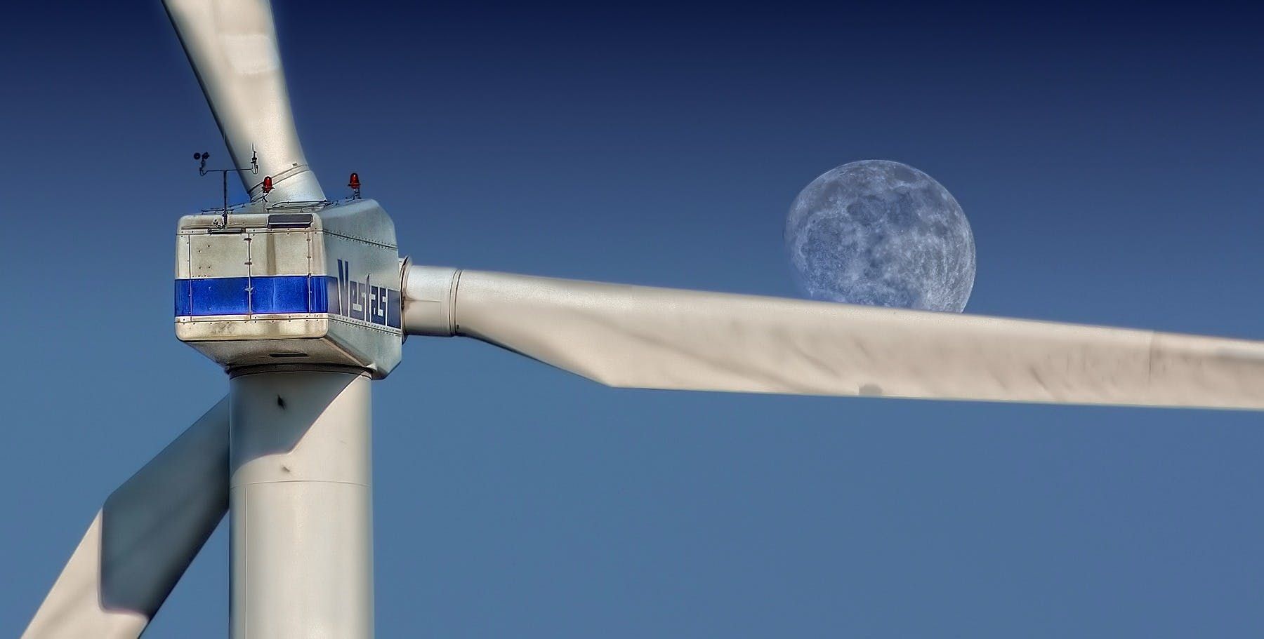 Wind turbine with blue and white blades against a clear blue sky; a translucent sphere is on one blade.