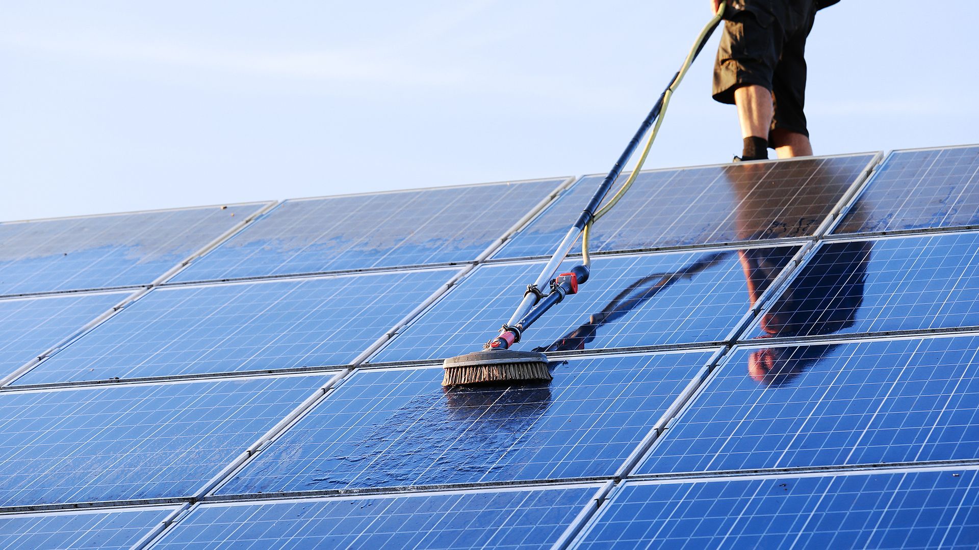 A row of solar panels against a cloudy sky with the sun shining through them.