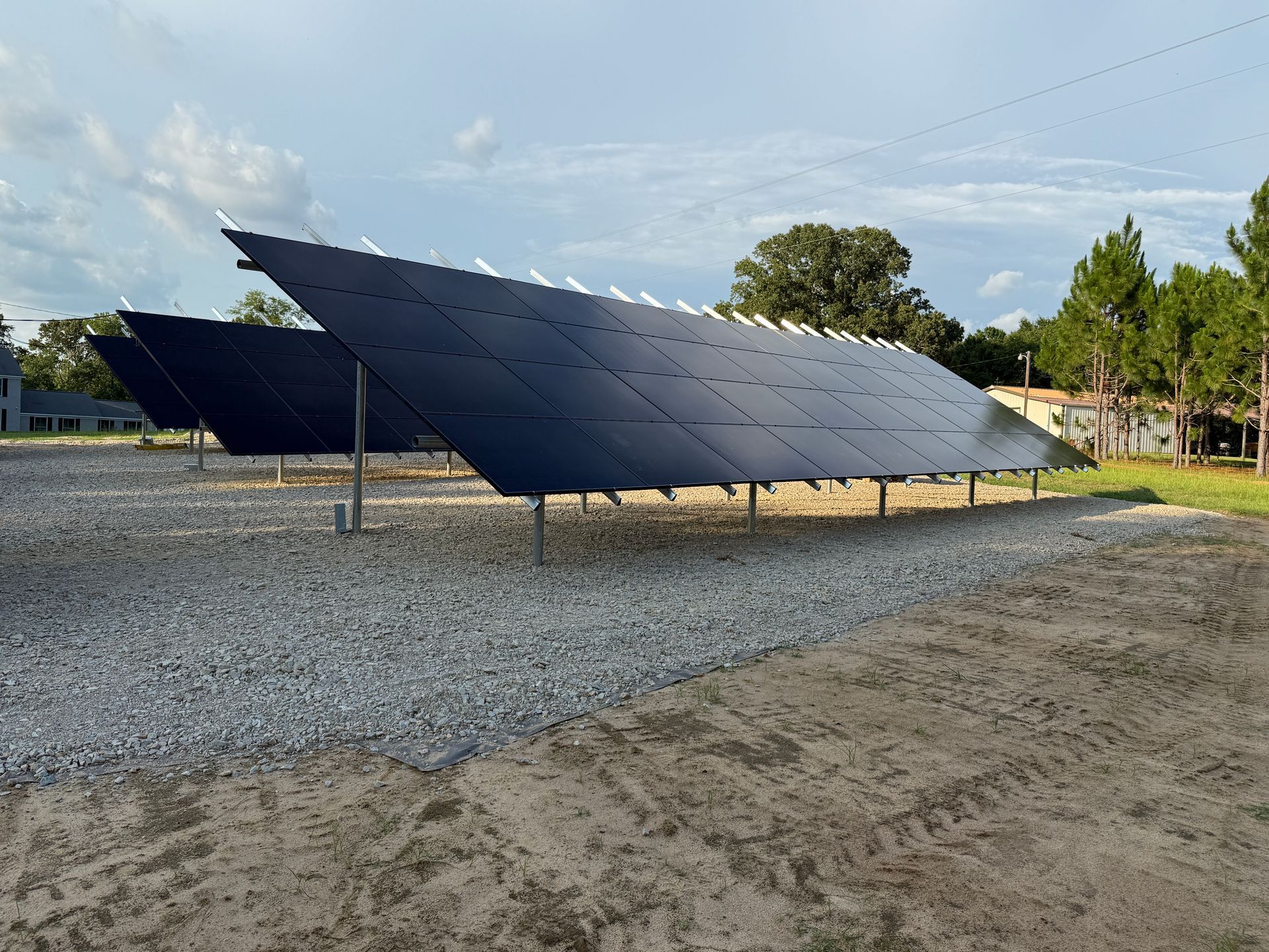 A row of solar panels against a cloudy sky with the sun shining through them.