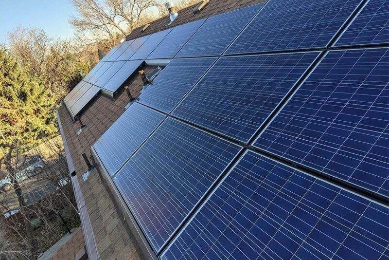 A row of solar panels against a cloudy sky with the sun shining through them.
