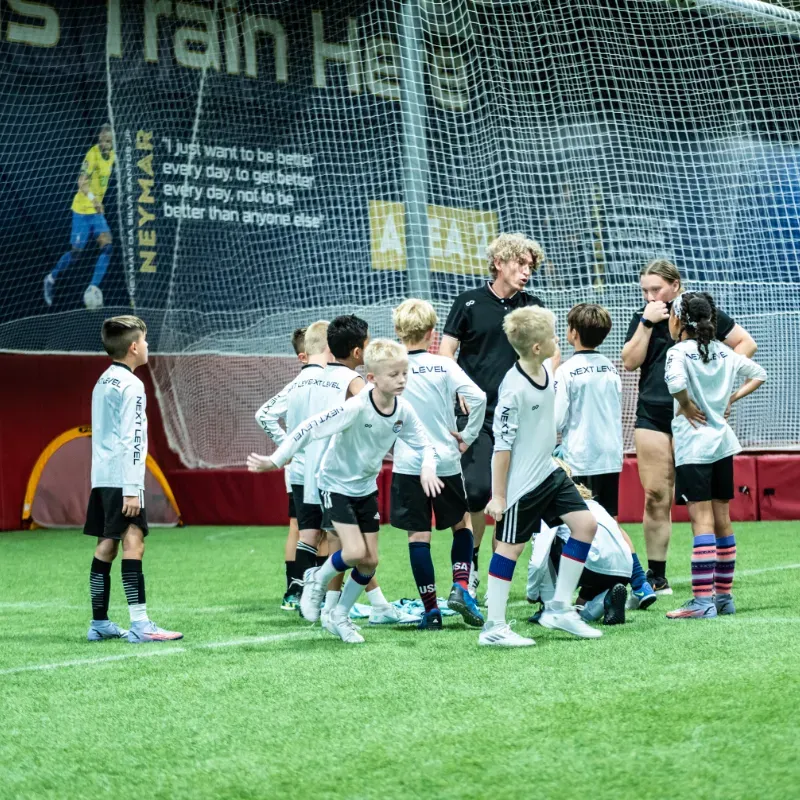 A group of young boys are standing on a soccer field in front of a sign that says train here