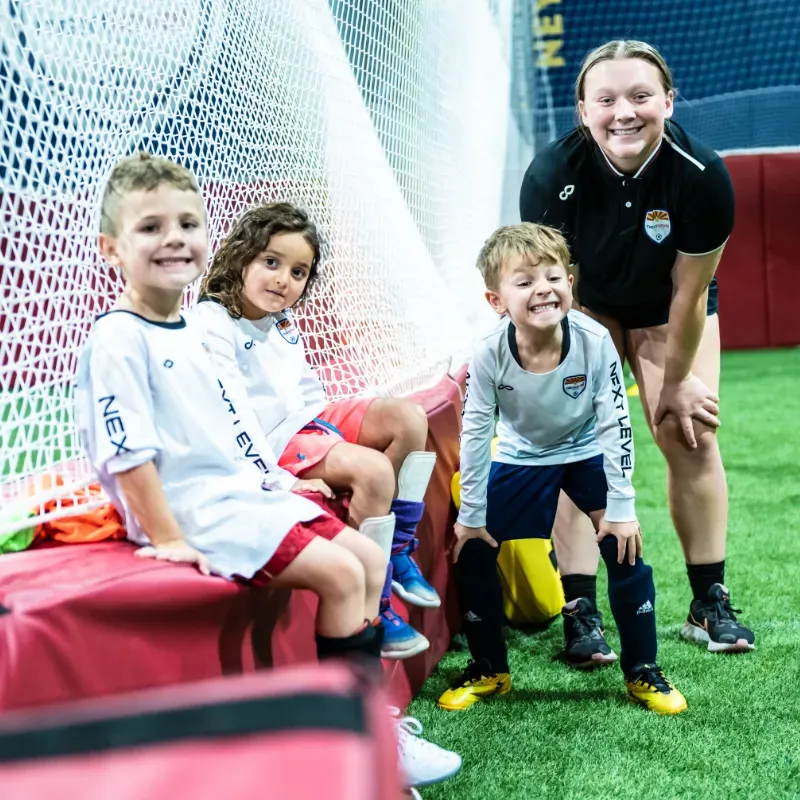 A group of children are sitting on a bench in front of a soccer goal.