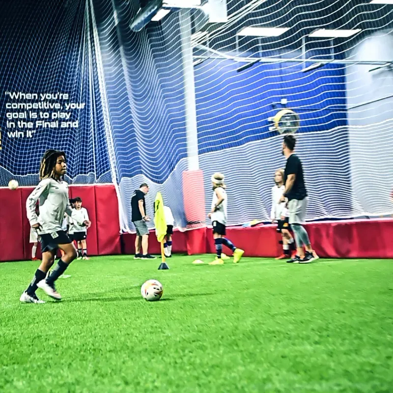 A group of children are playing soccer in an indoor gym.