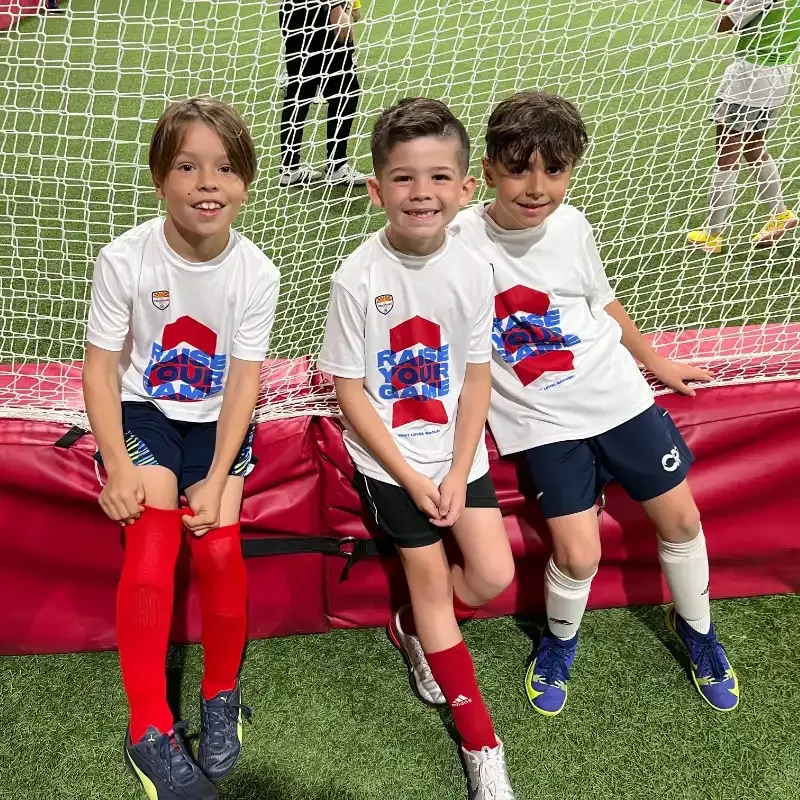 Three young boys are sitting next to each other on a soccer field.