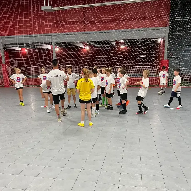 A group of children are playing soccer in a gym.