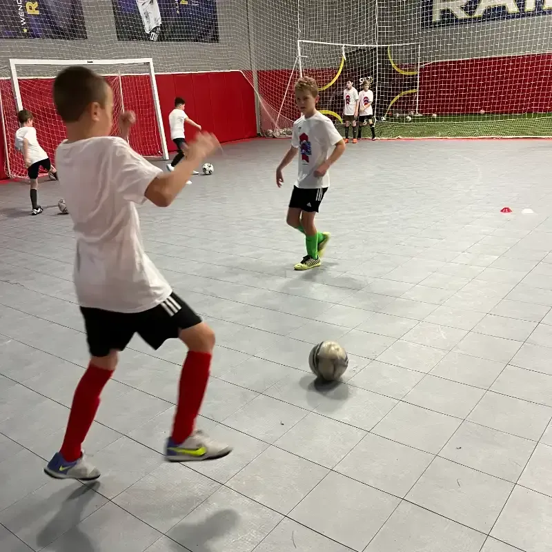 A group of young boys are playing soccer on a tiled floor