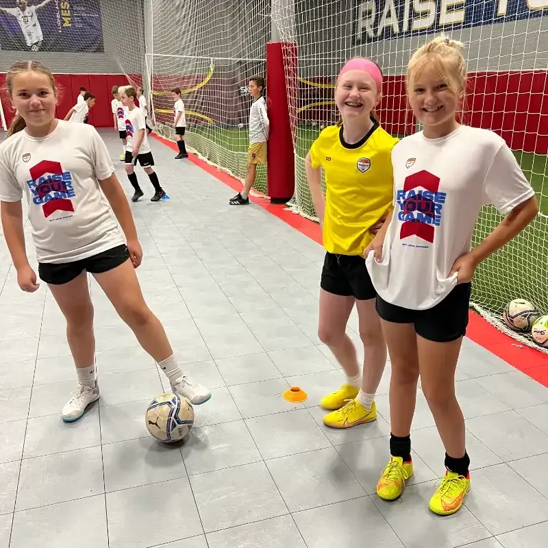 A group of young girls are standing in front of a soccer goal.