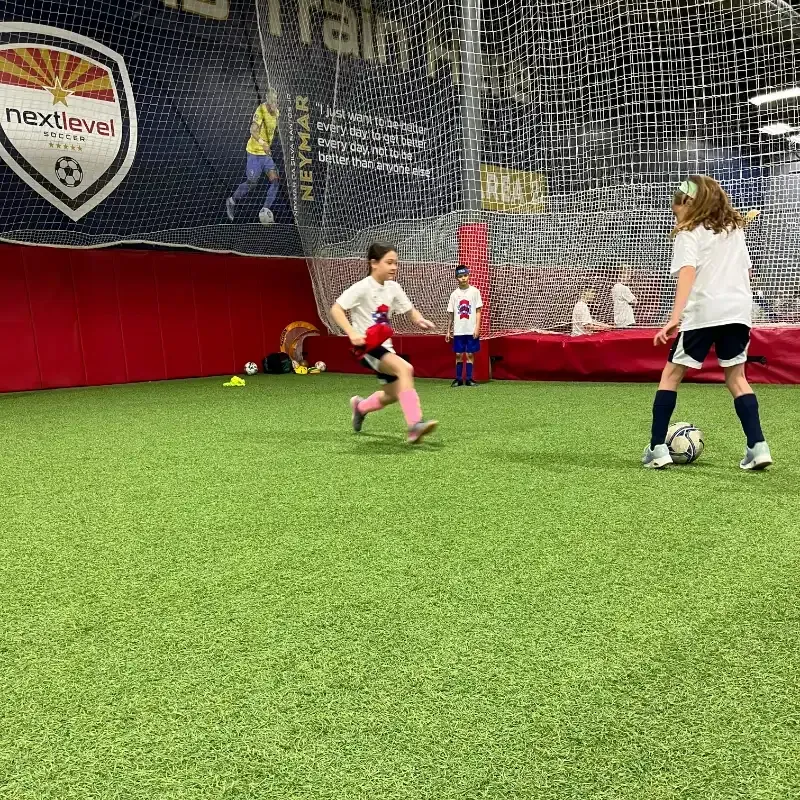 A group of young girls are playing soccer on a indoor field.