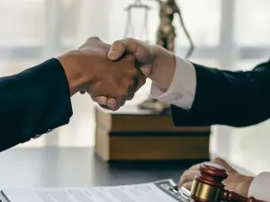 A judge and a lawyer are shaking hands in front of a statue of justice.