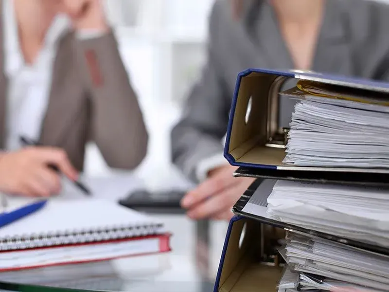 A woman is sitting at a desk with a stack of binders.