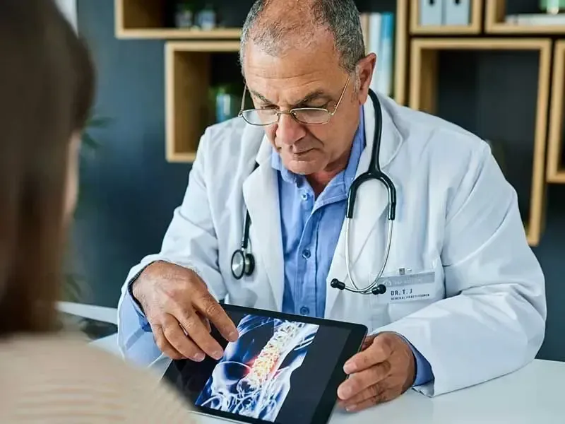 A doctor is looking at a tablet screen while talking to a patient.