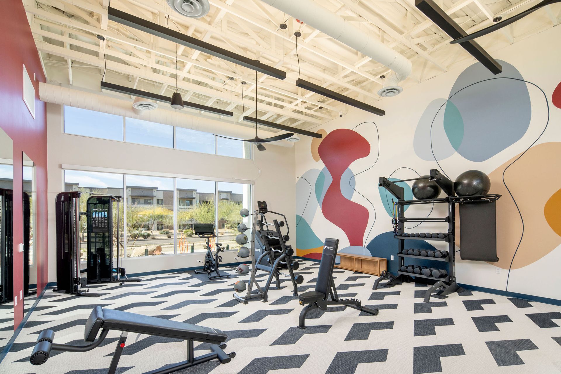 A gym with a lot of exercise equipment and a mural on the wall.