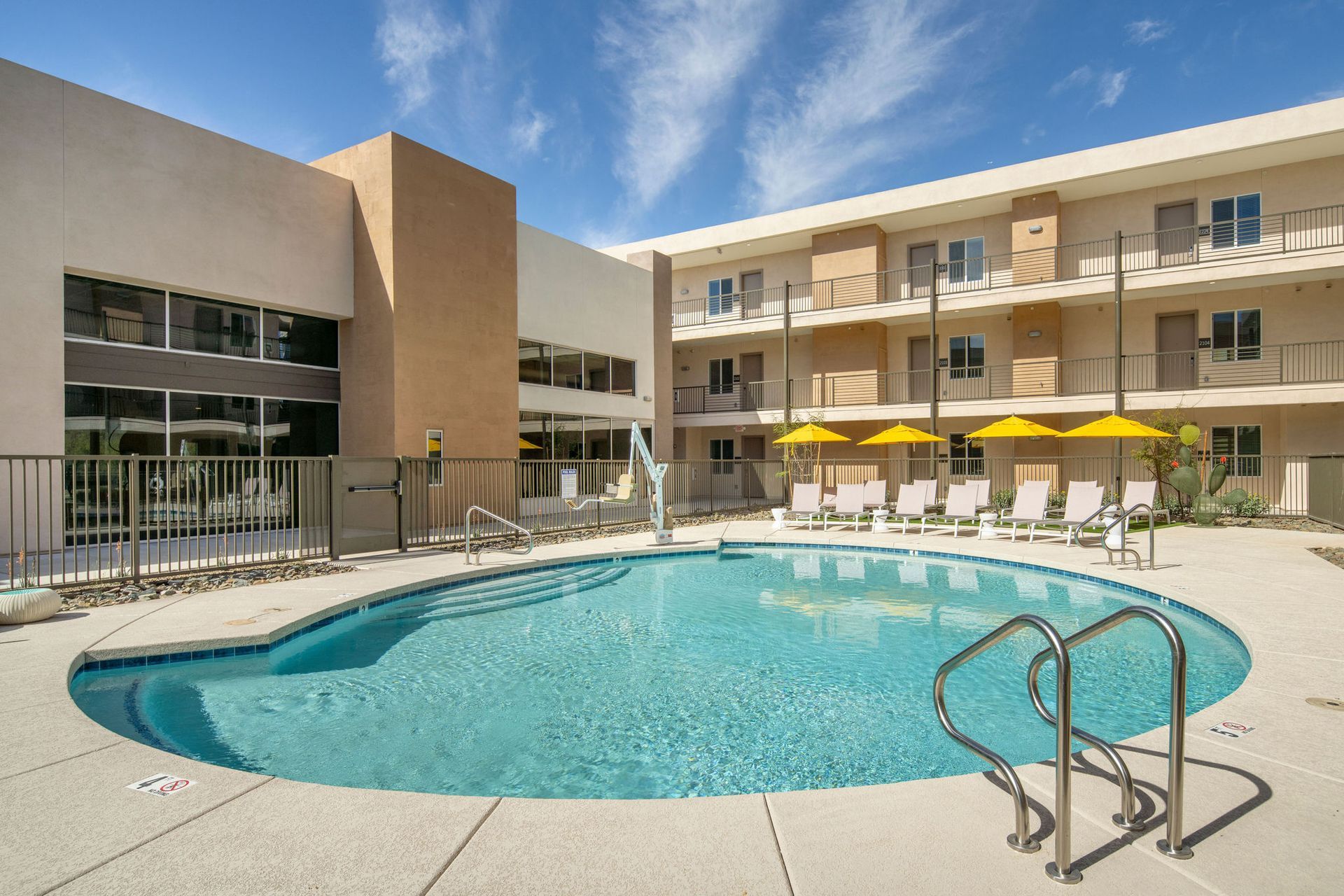 A large swimming pool surrounded by chairs and umbrellas in front of a building.