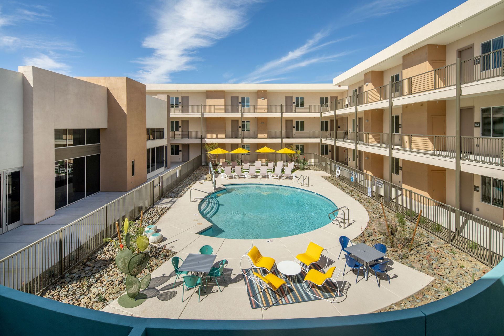 An aerial view of a hotel with a large swimming pool surrounded by chairs and tables.