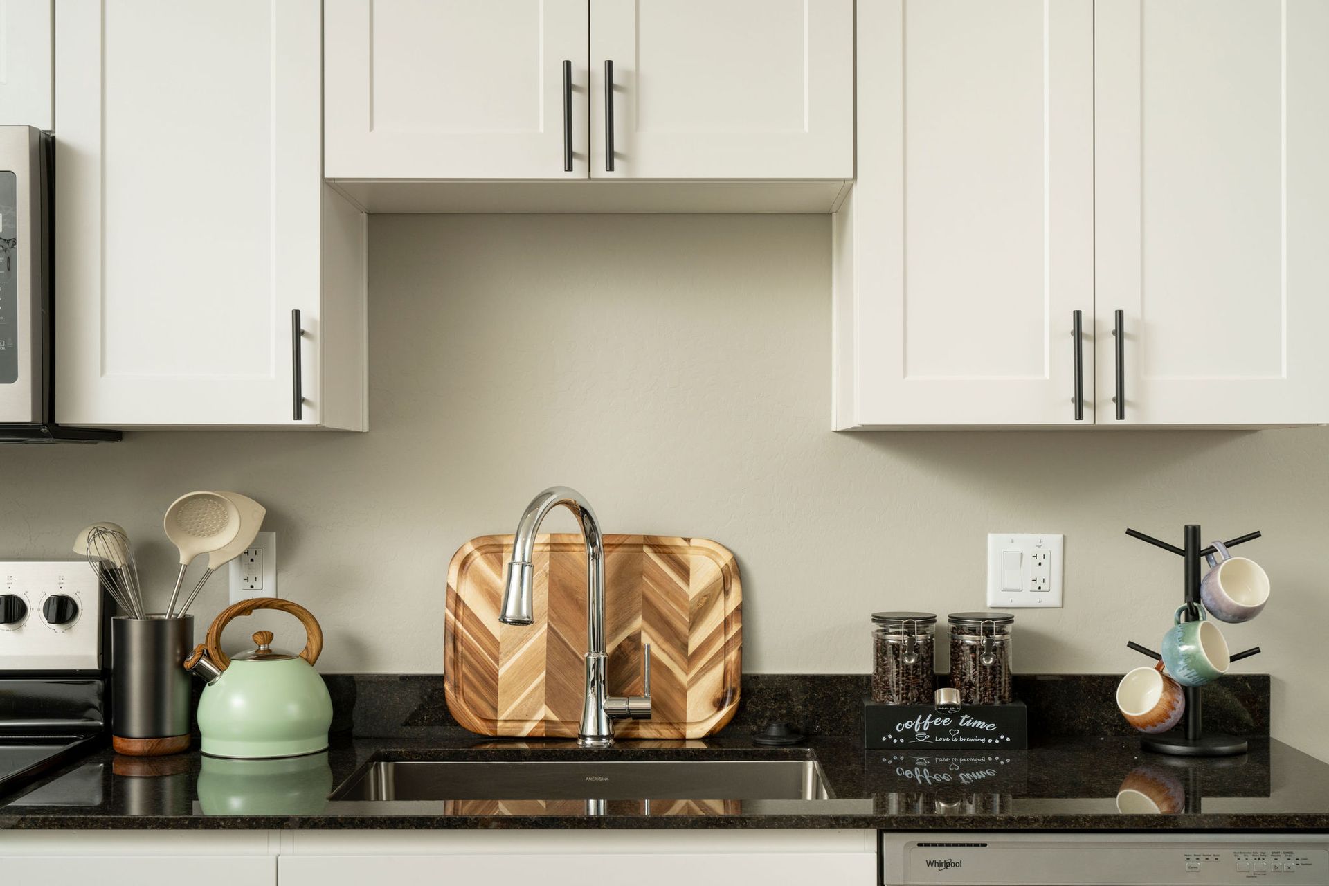 Kitchen with white cabinets, black countertop, and stainless steel sink with cutting board.