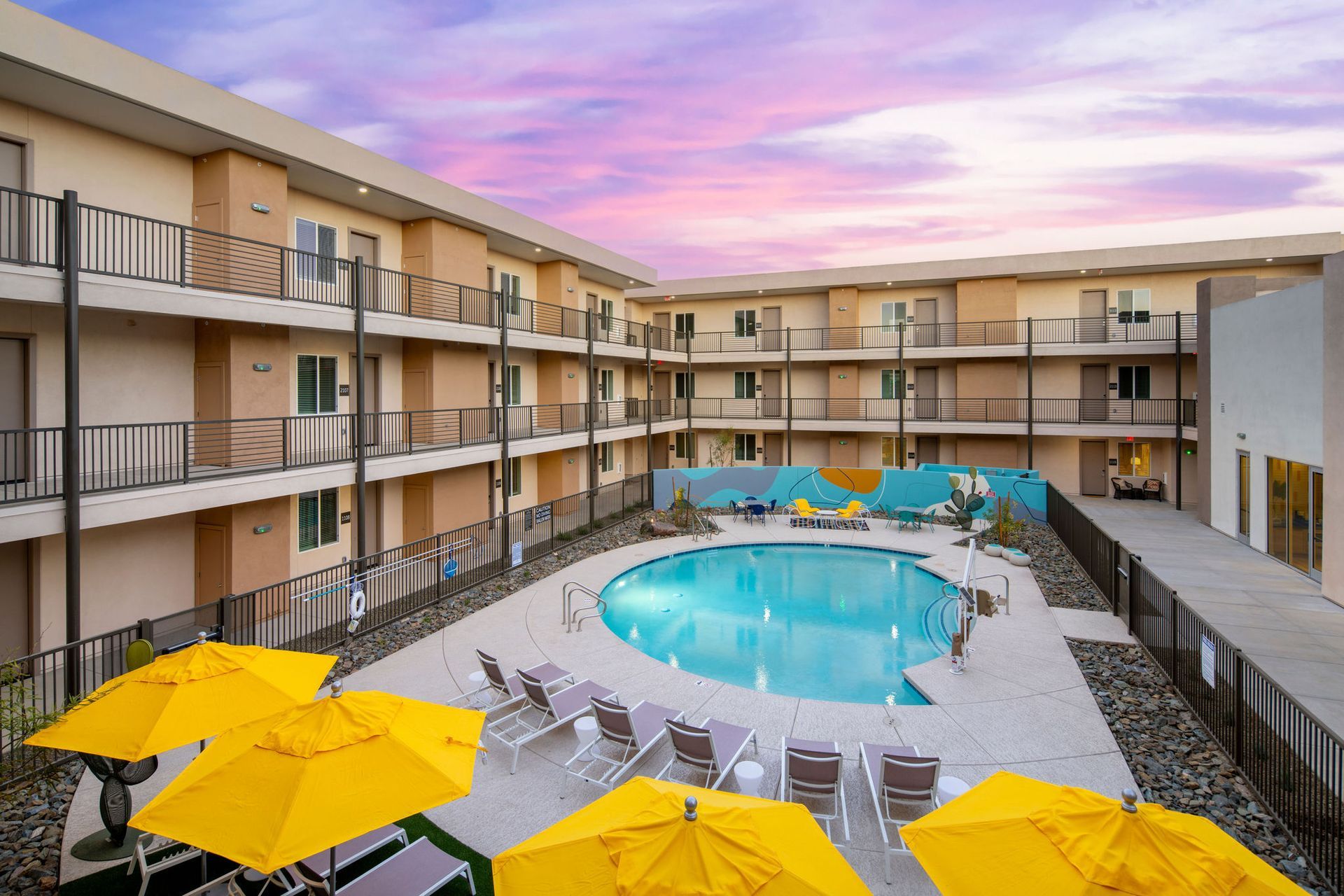 Apartment community with a large swimming pool surrounded by yellow umbrellas and chairs.