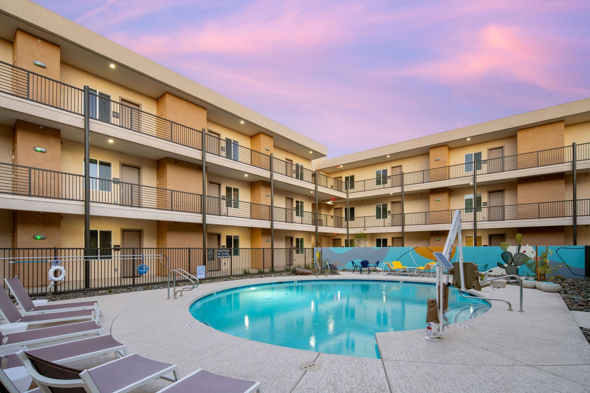 Hotel courtyard with pool, surrounded by multi-story buildings. Sunset sky.