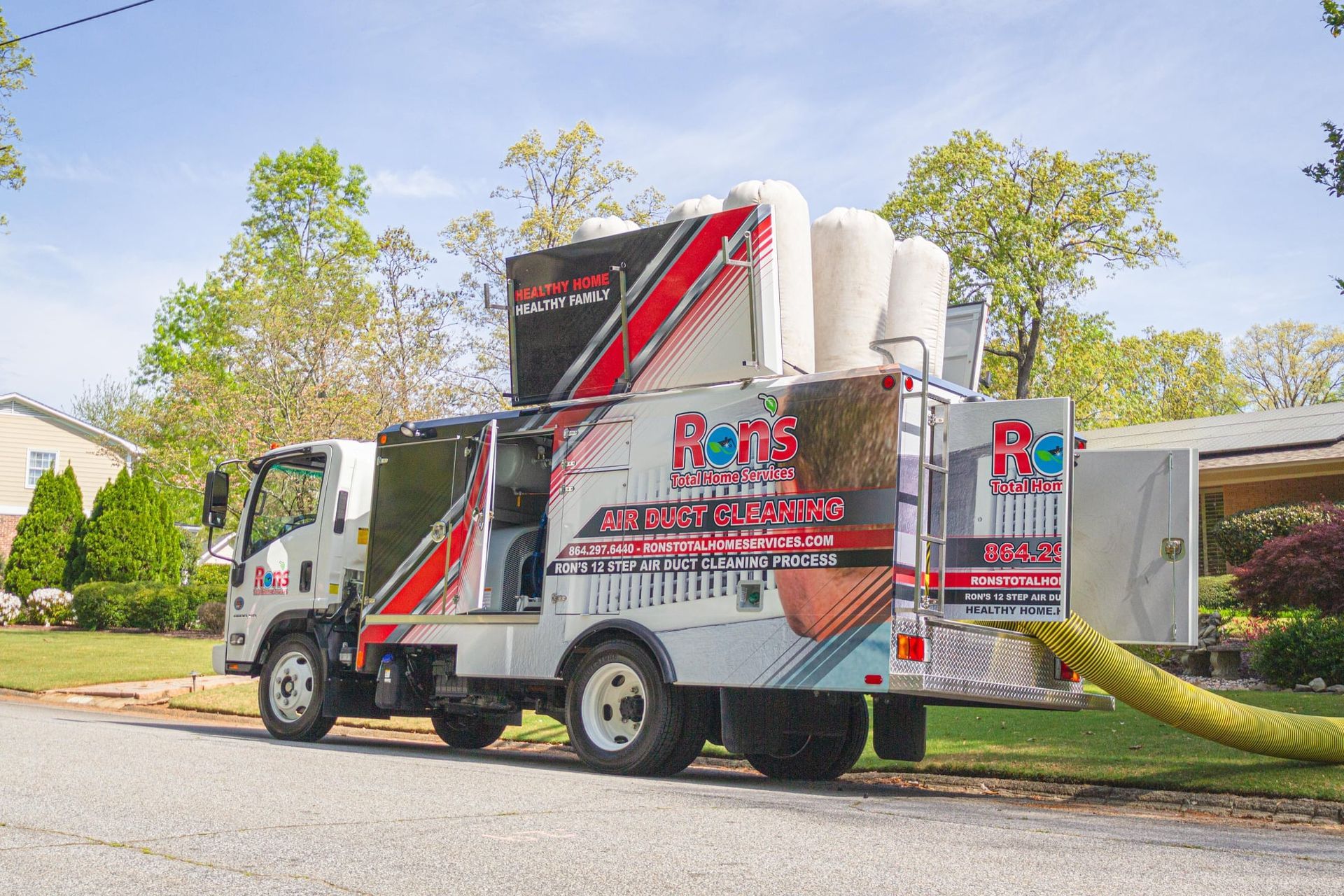 A Ram Insulation truck parked on a residential street, with a yellow hose extending toward a home under clear blue skies.