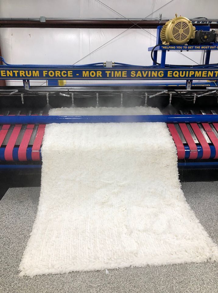 A white shag rug being cleaned on an industrial Centrum Force machine with pink conveyor belts.