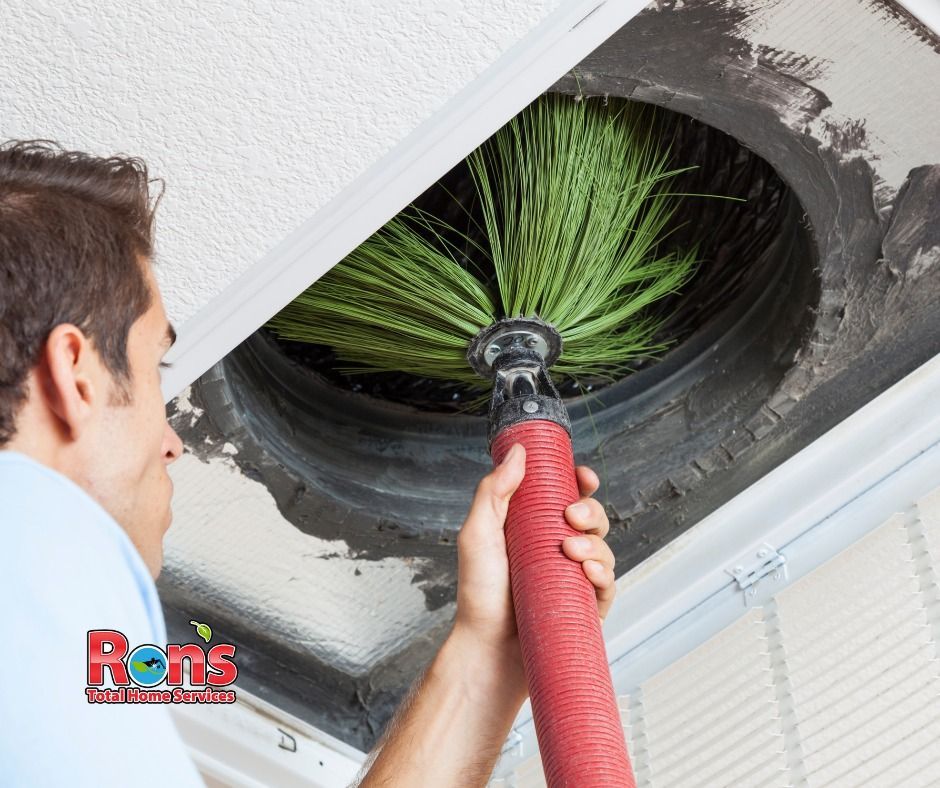 A technician uses a rotating brush tool to clean a round ceiling air duct.