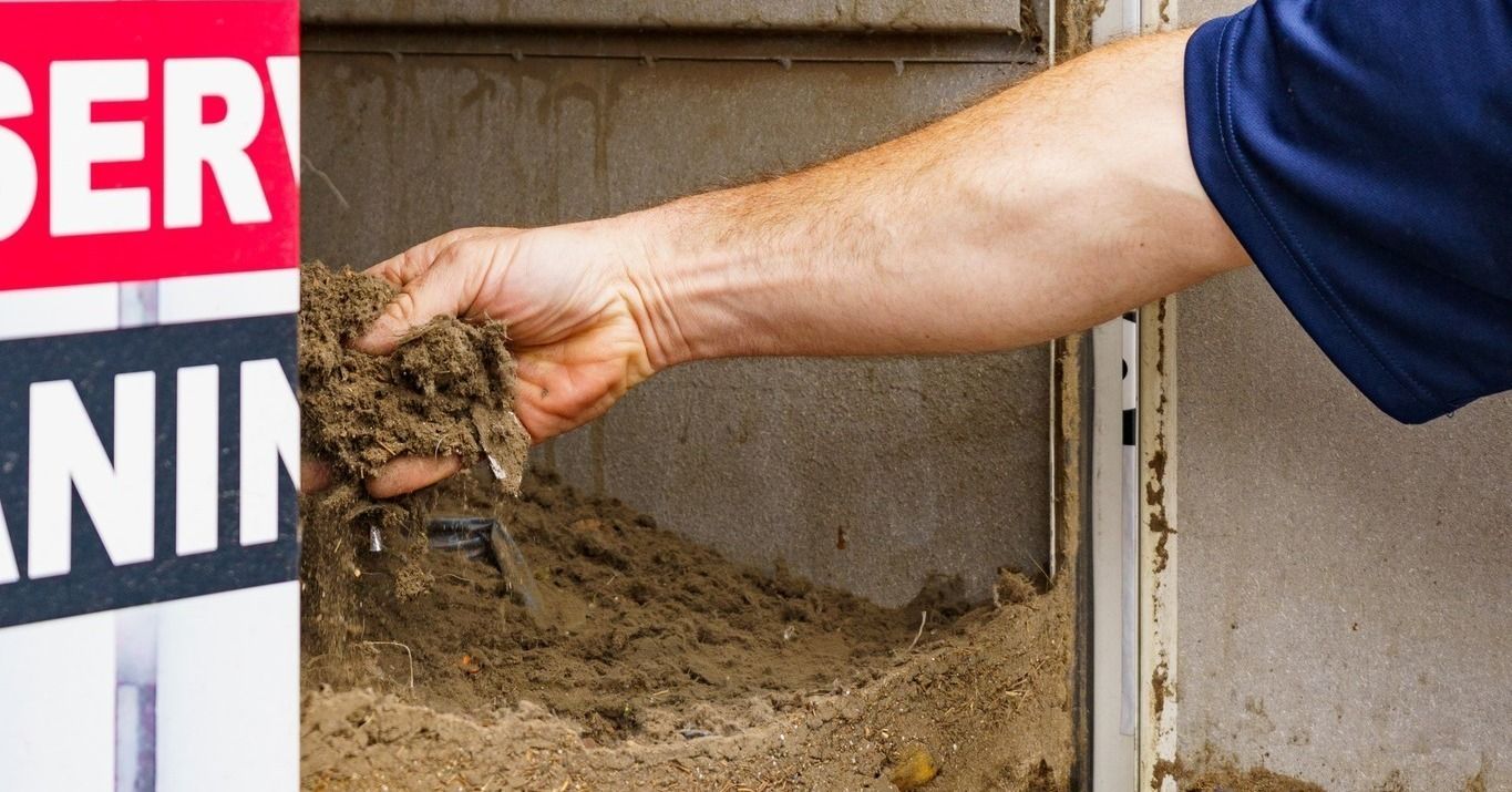 A person's hand reaches into a pile of dirt or insulation material next to a sign with red and white text.