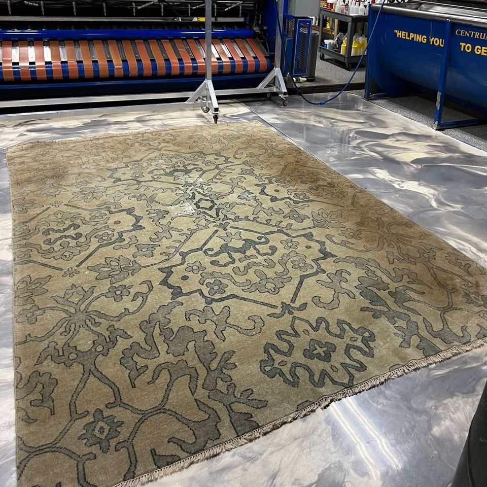 A neutral-toned area rug with a dark grey, intricate floral pattern laid out on a polished grey concrete floor.