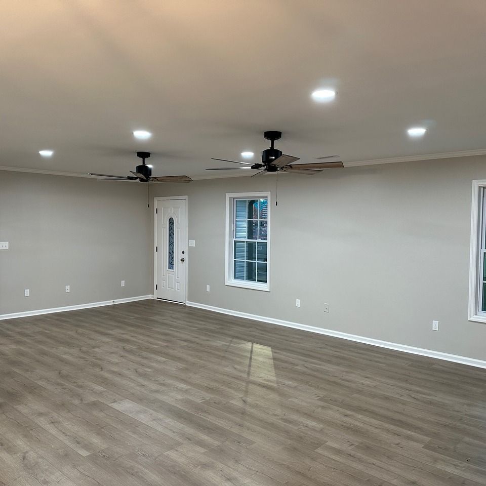 A spacious room with light gray walls, wood-look flooring, two ceiling fans, recessed lighting, and a white front door.