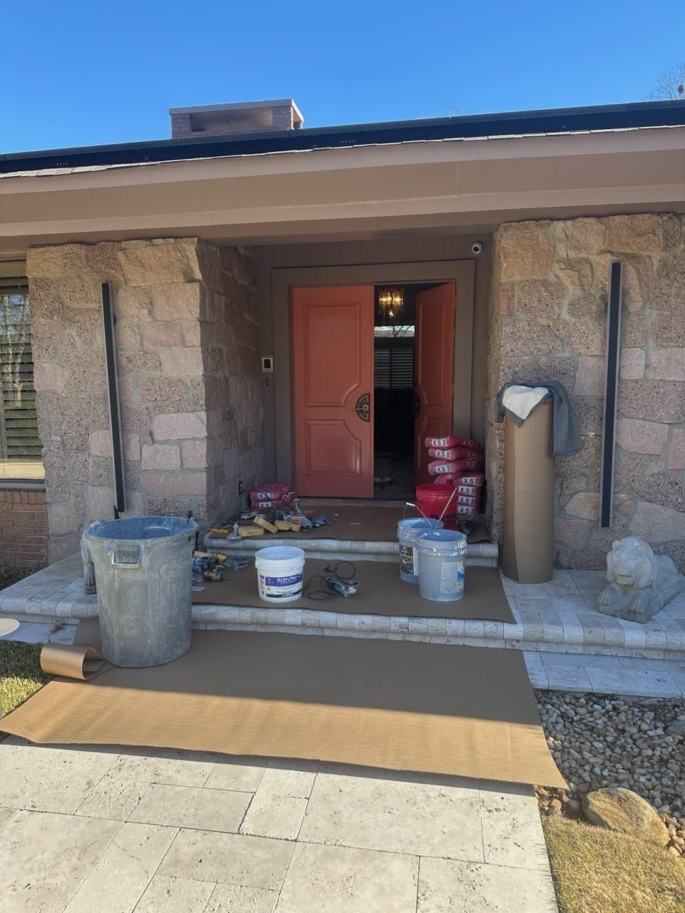 Exterior view of a home entrance with a peach double door, stone walls, construction materials, and floor protection.