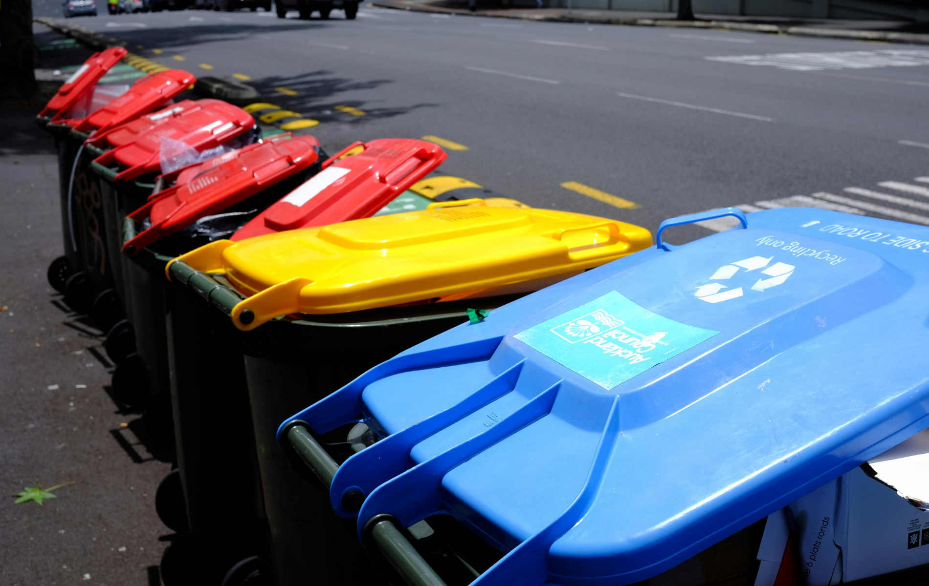 A row of colorful trash and recycling bins lined up along a sidewalk next to a street.