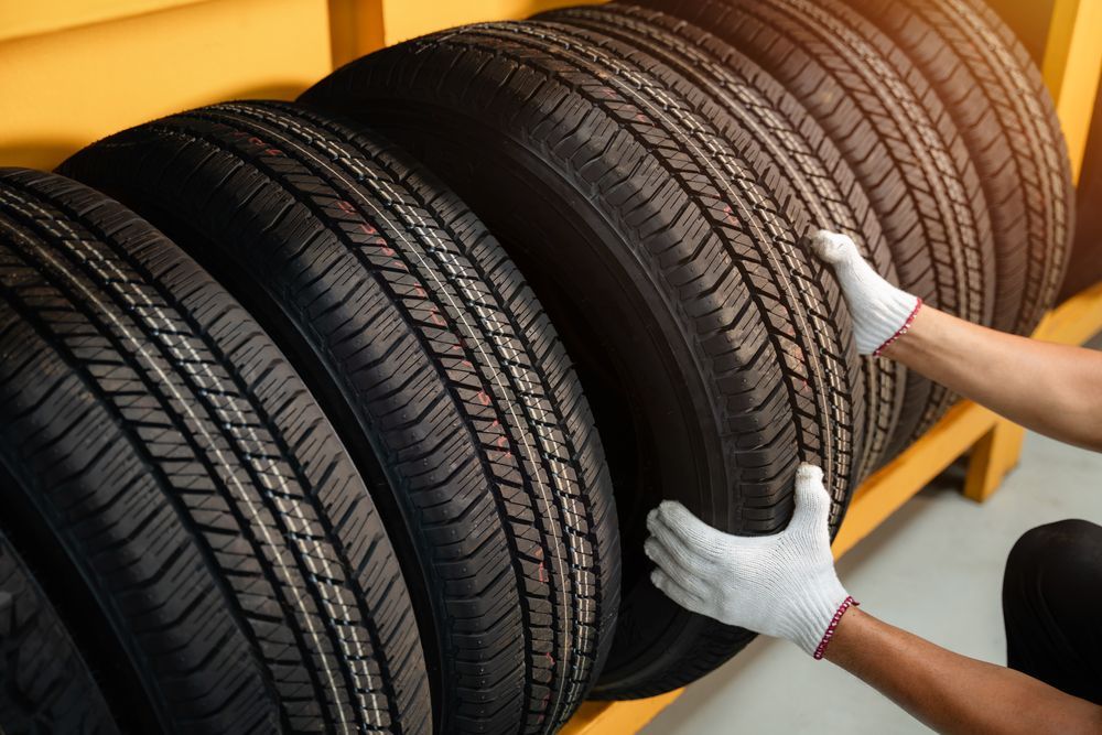 A Person Lifts a Black Car Tire from A Rack in A Warehouse — Morisset Automotive in Morisset, NSW