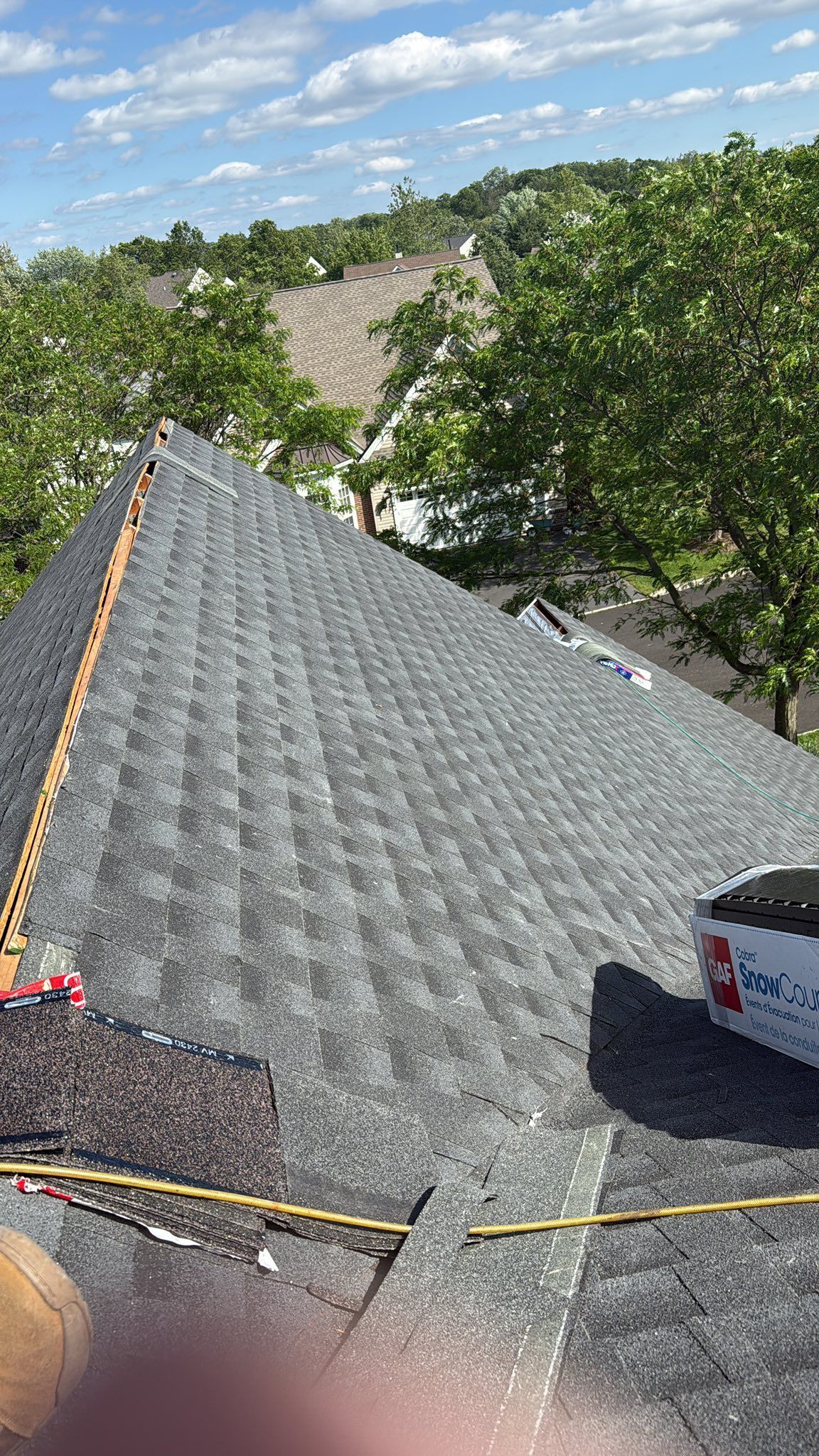 A dark gray shingled roof under construction on a sunny day with trees in the background.