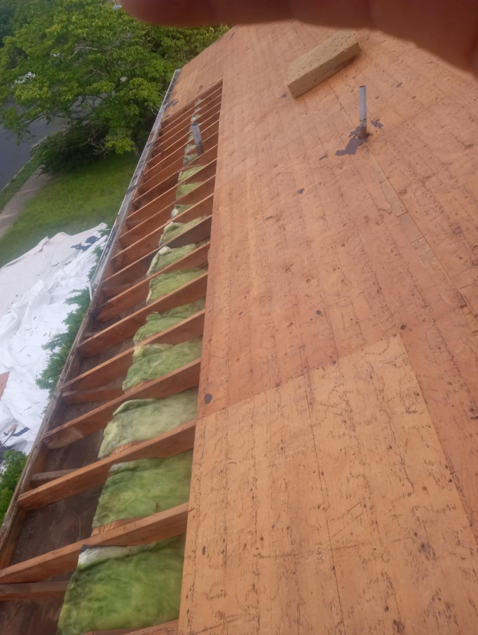 Roof partially disassembled, showing rafters, insulation, and exposed plywood.