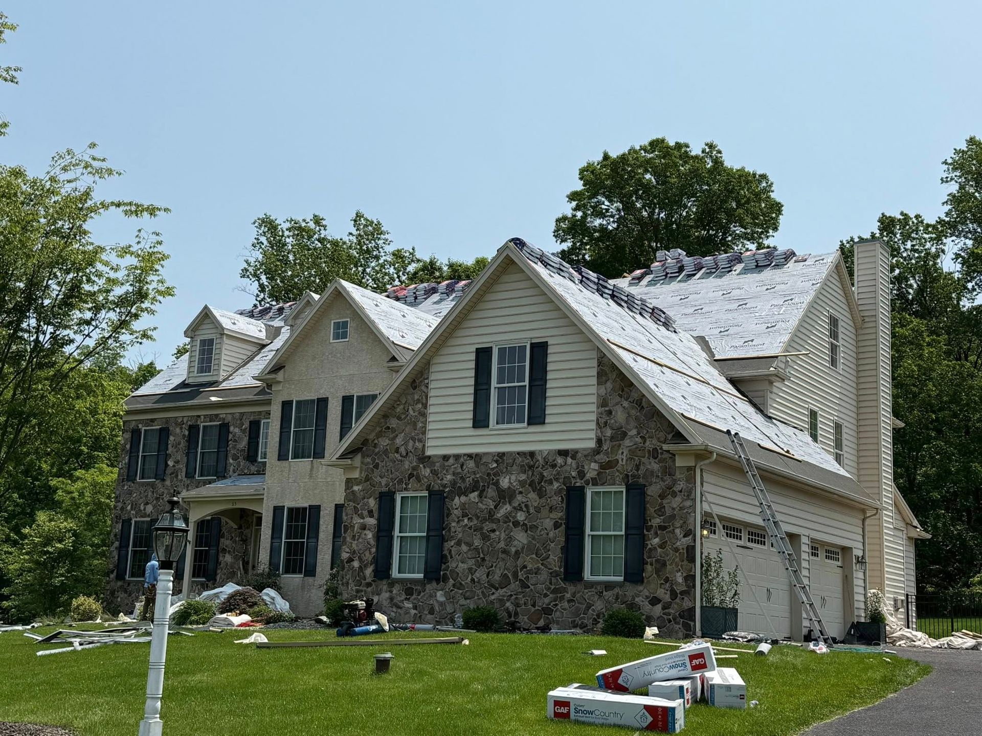 House with partial roof replacement; workers, blue sky, green grass, and trees.