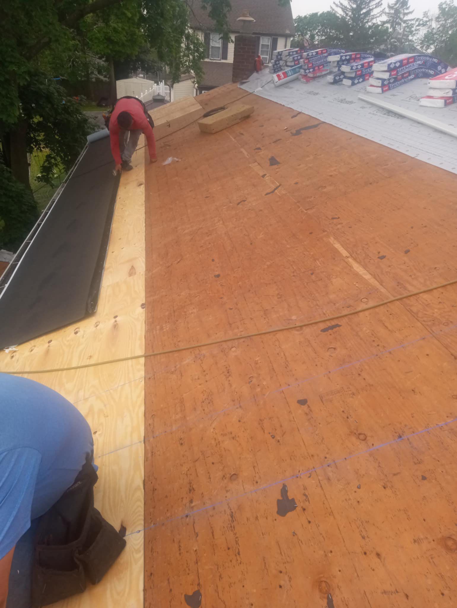 Roofers installing roofing material on a slanted roof outdoors. One roofer is working on the edge with the other one nearby.