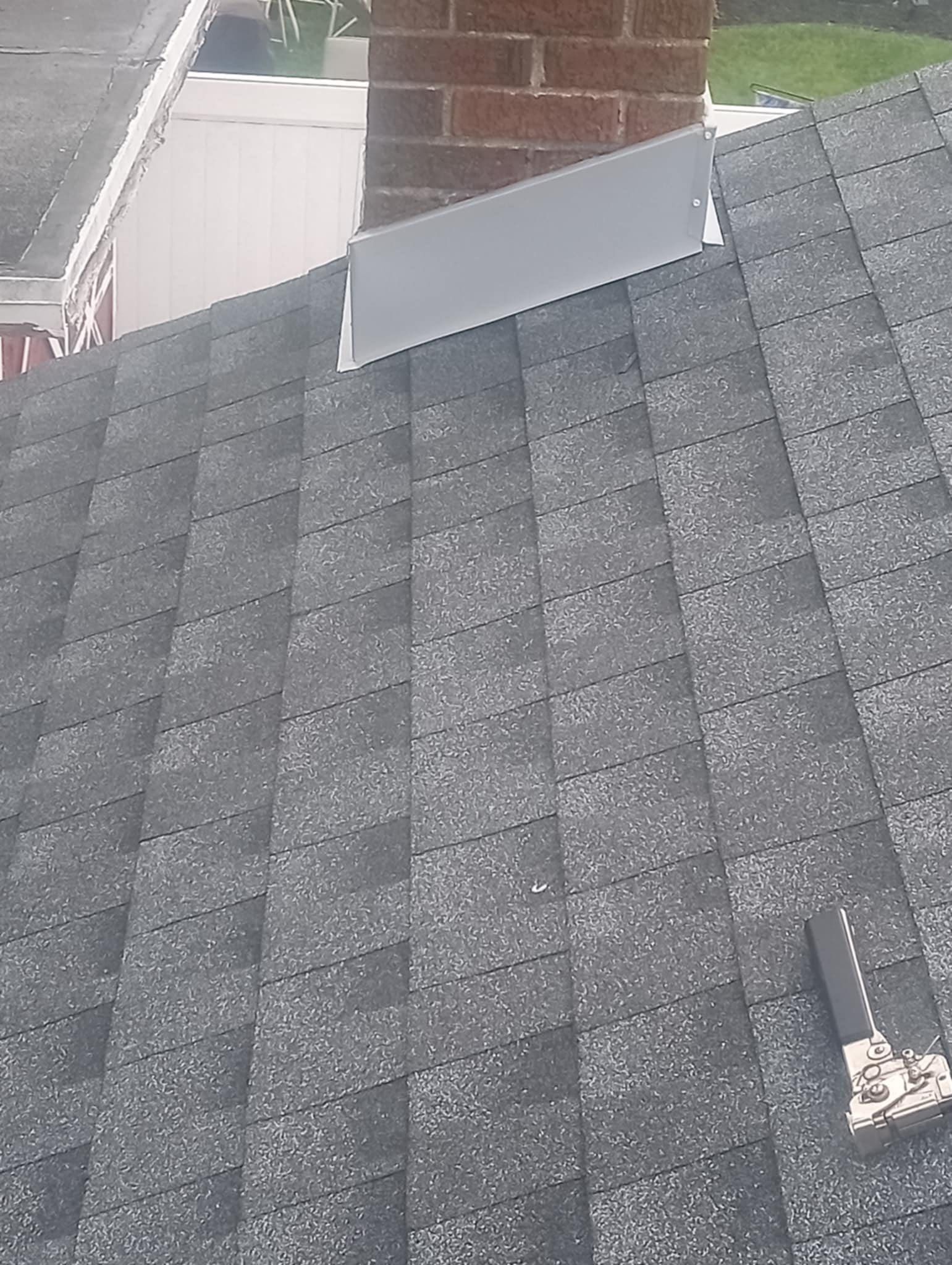 Gray asphalt shingle roof with silver flashing against a brick chimney.