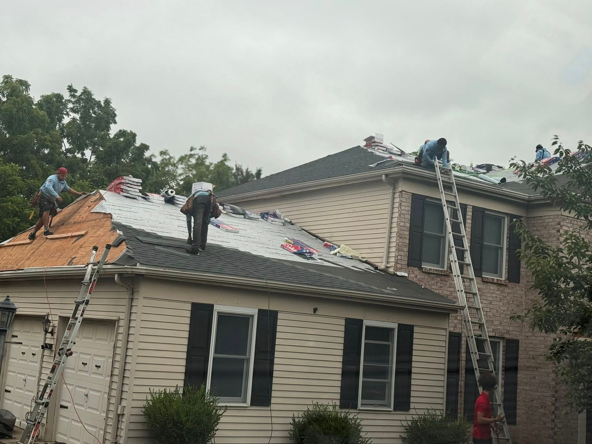 Roofers working on a residential house with ladders, removing old roofing, cloudy day.