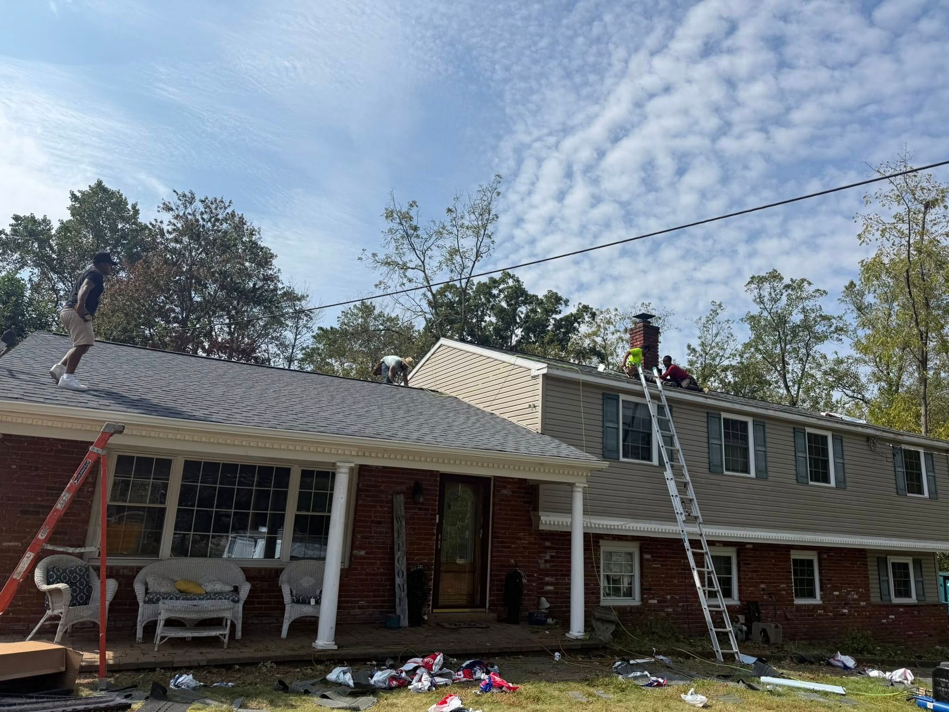 Roofers working on a two-story house with a red brick facade, under a partly cloudy sky.