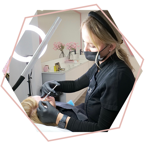 A woman wearing a mask and gloves is getting a tattoo on a woman 's face.