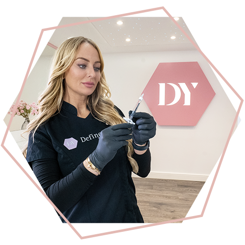 A woman is holding a syringe in front of a pink sign that says dy.