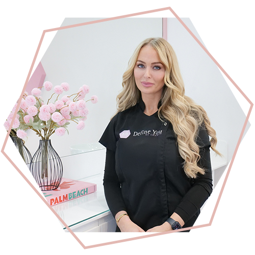 A woman in a black shirt is standing in front of a vase of pink flowers.