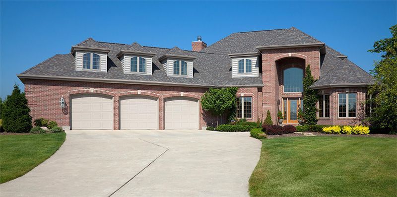 A large brick house with three garage doors and a driveway