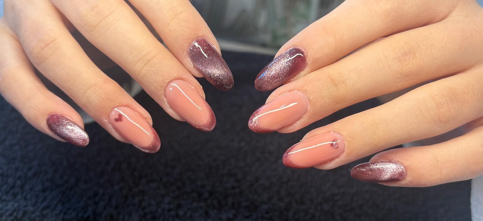 Mani con unghie a mandorla dipinte in una combinazione di colori rosa chiaro e bordeaux, con piccoli cuori e dettagli lineari.