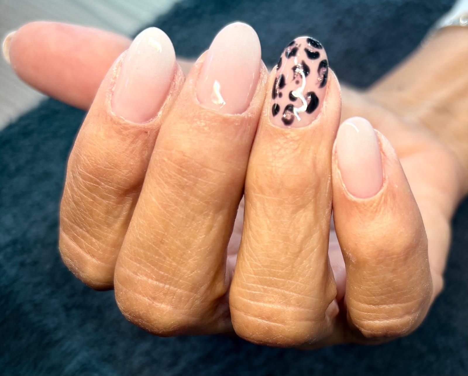 Mano con unghie ovali. Tre sono rosa chiaro, una è trasparente e una ha un motivo leopardato.