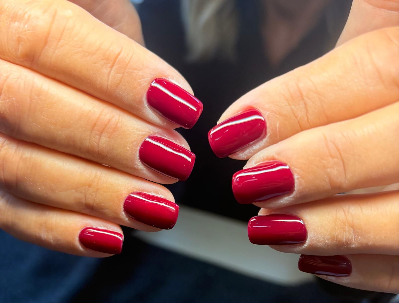 Mani con smalto rosso corto, esposte su uno sfondo chiaro.